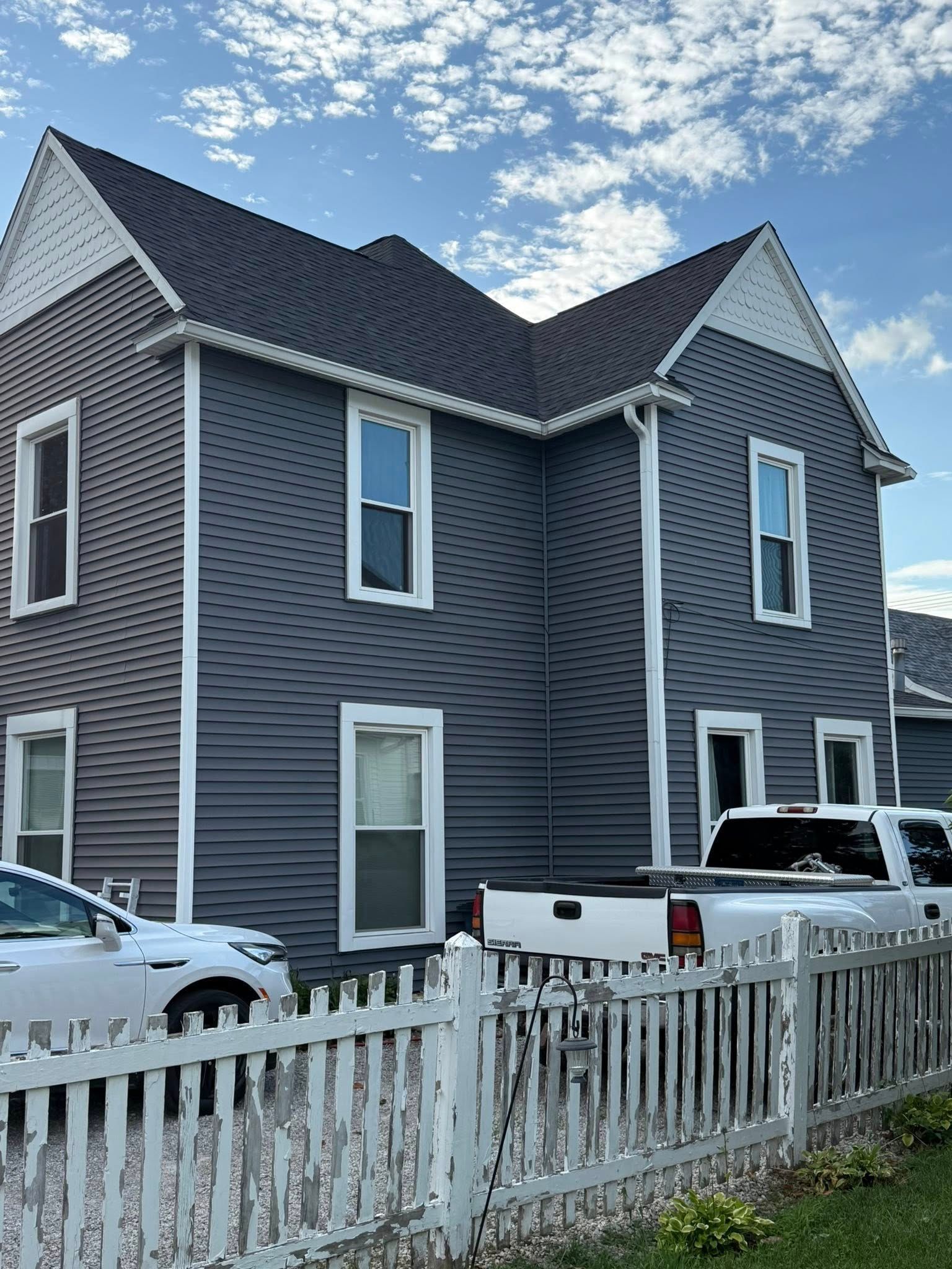 Gray house with white trim, a white picket fence, and parked vehicles.