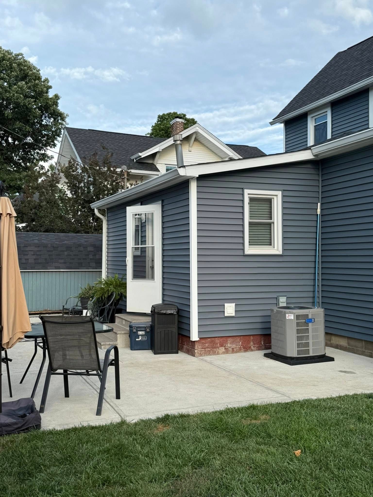 Back patio of a blue house with white trim, concrete patio, lawn, and an air conditioner.