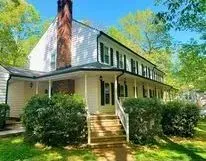 Two-story white house with black shutters, wraparound porch, wooden stairs, and large brick chimney.