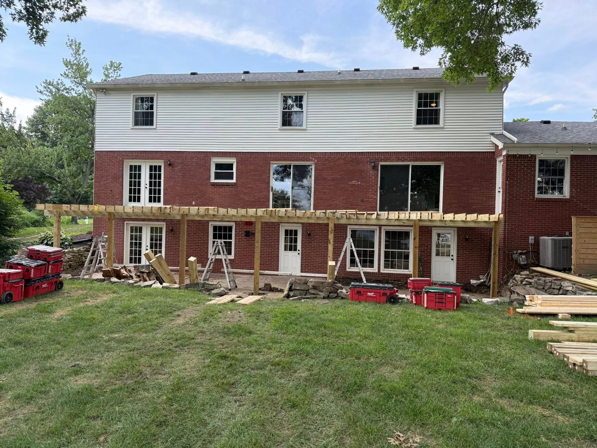 Back of a two-story brick house under construction, with a partially built wooden deck in the backyard.
