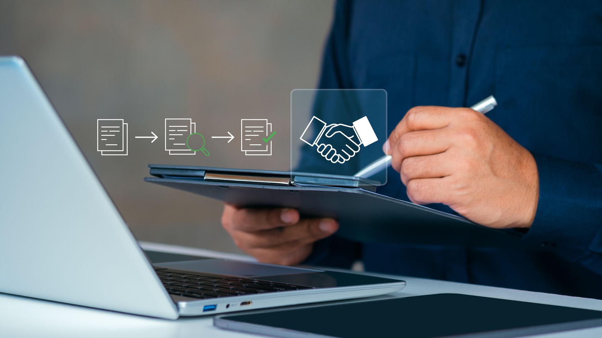 Hand using tablet beside laptop, with digital handshake icons over a blue background.