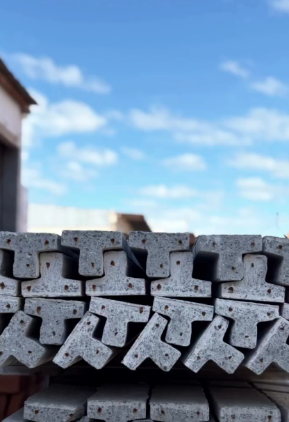 Vigas metálicas grises apiladas al aire libre contra un cielo azul con nubes.
