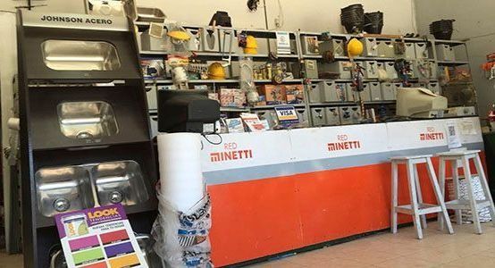 Mostrador de una pequeña tienda con frontal naranja, taburetes y estanterías con artículos variados detrás.