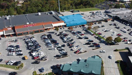 Aerial view of a crowded parking lot beside a shopping center with orange and blue roofs.
