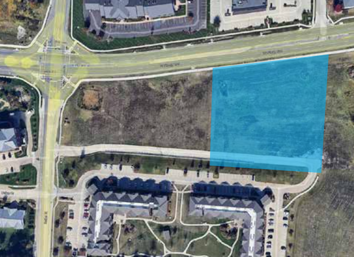 Aerial view of a neighborhood lot highlighted in blue beside roads and apartment buildings.