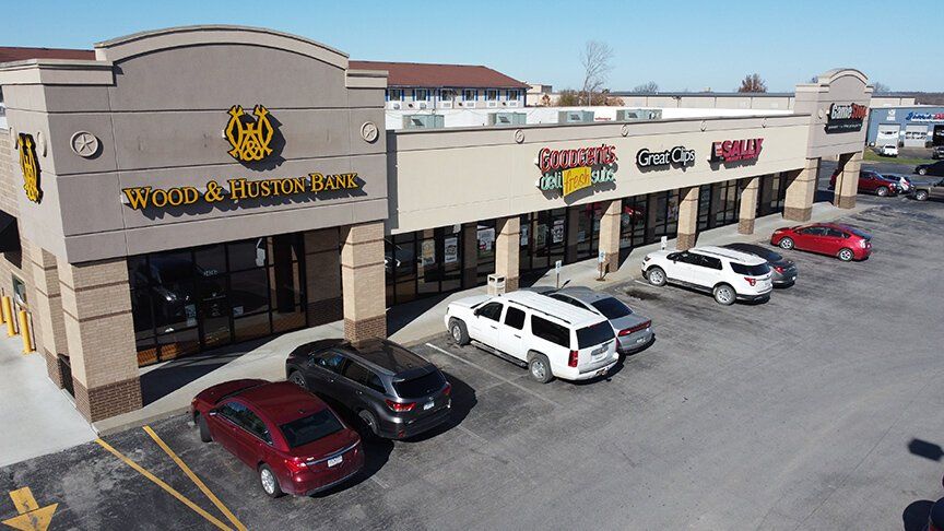 Strip mall storefronts with parked cars in a sunny shopping center parking lot | Sedalia Square