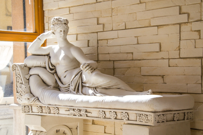 Una statua in marmo bianco raffigurante una figura sdraiata su una panca decorata e imbottita.
