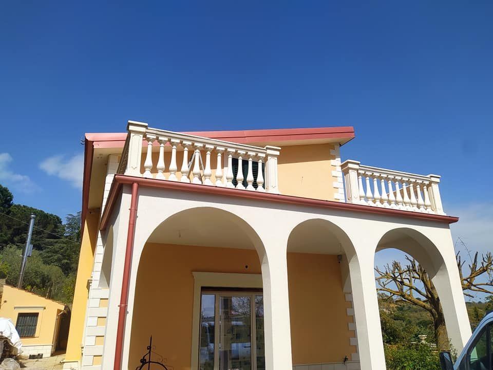 Una casa con archi in pietra bianca e una terrazza con una balaustra bianca che si staglia contro un cielo azzurro e terso.