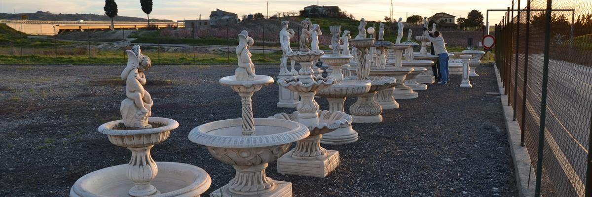 Una fila di fontane in pietra bianca a più livelli in un terreno ghiaioso all'aperto al tramonto.