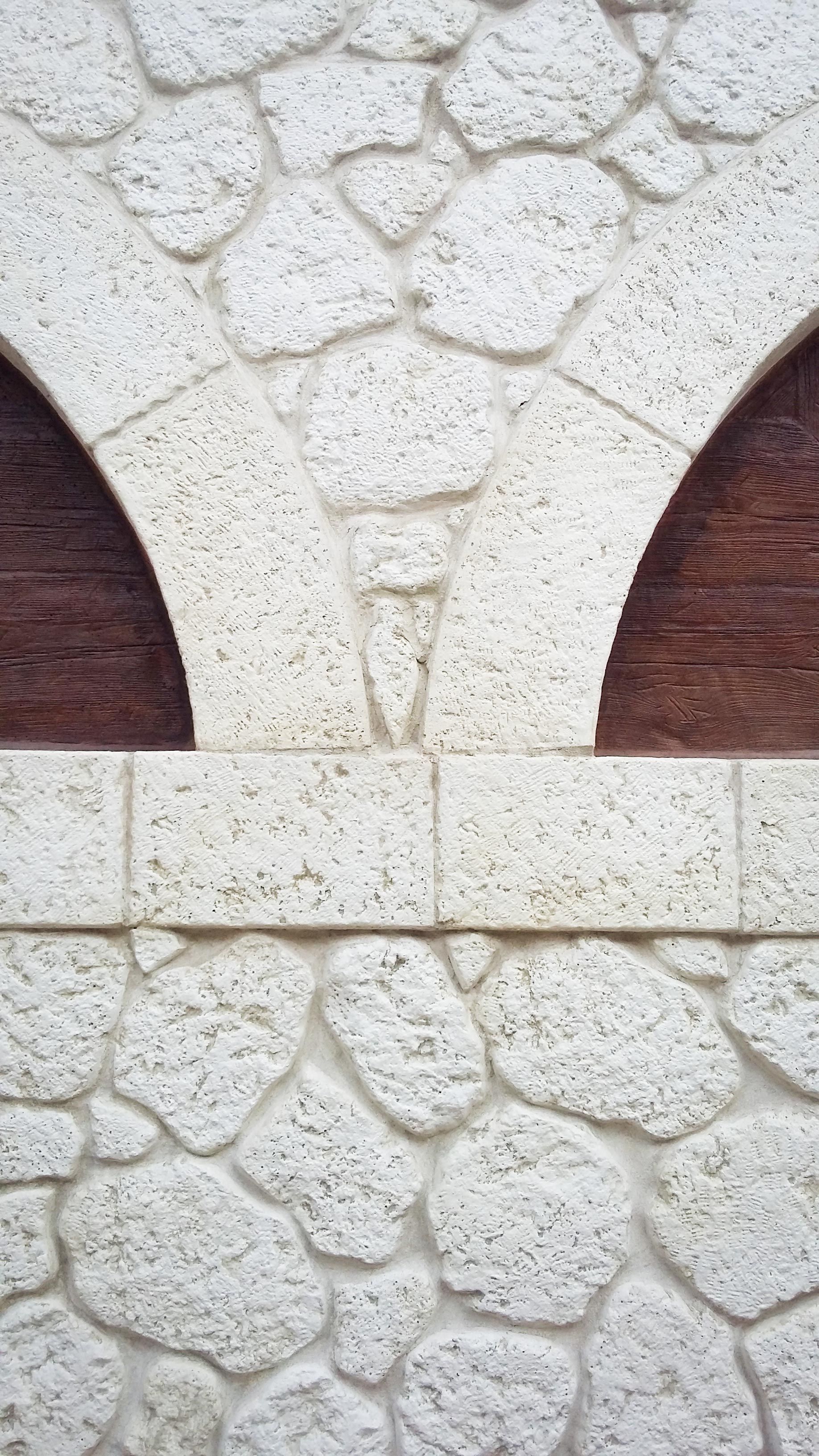 Un muro in pietra con due aperture ad arco, caratterizzato da una muratura in pietra bianca testurizzata.