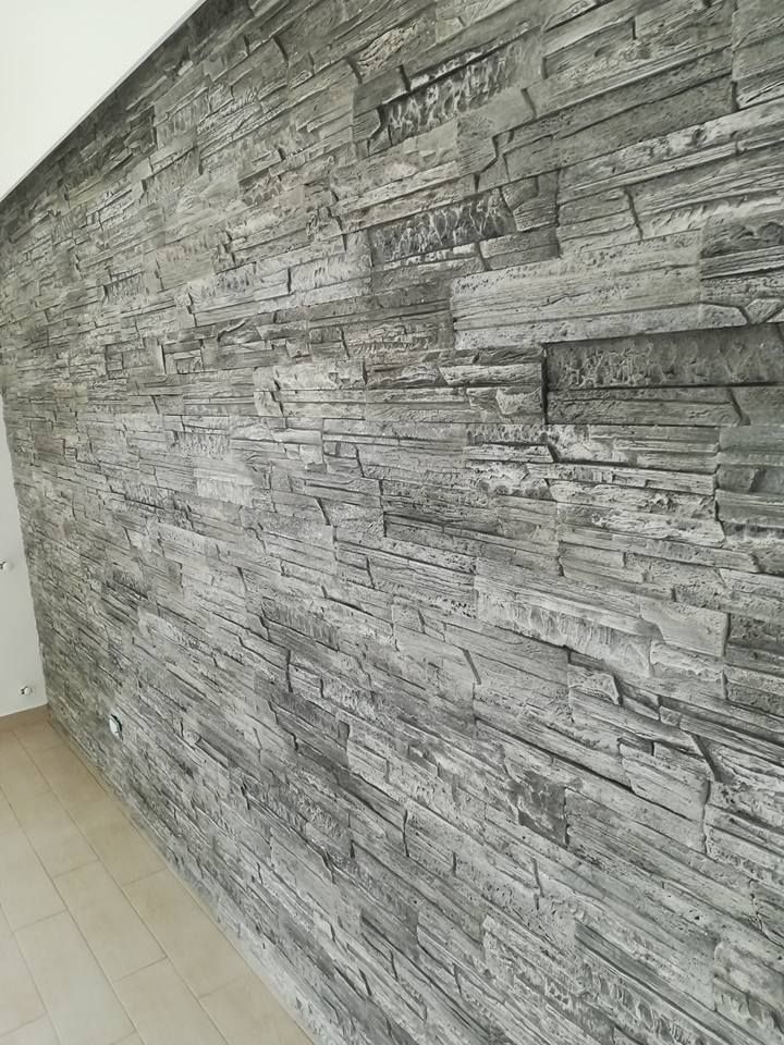 Una parete rivestita con rivestimento in pietra grigia impilati, che parte da un pavimento in legno chiaro.