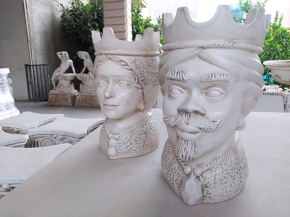 Due vasi decorativi in ceramica a forma di testa di re e regina con corone sono appoggiati su una superficie all'aperto.