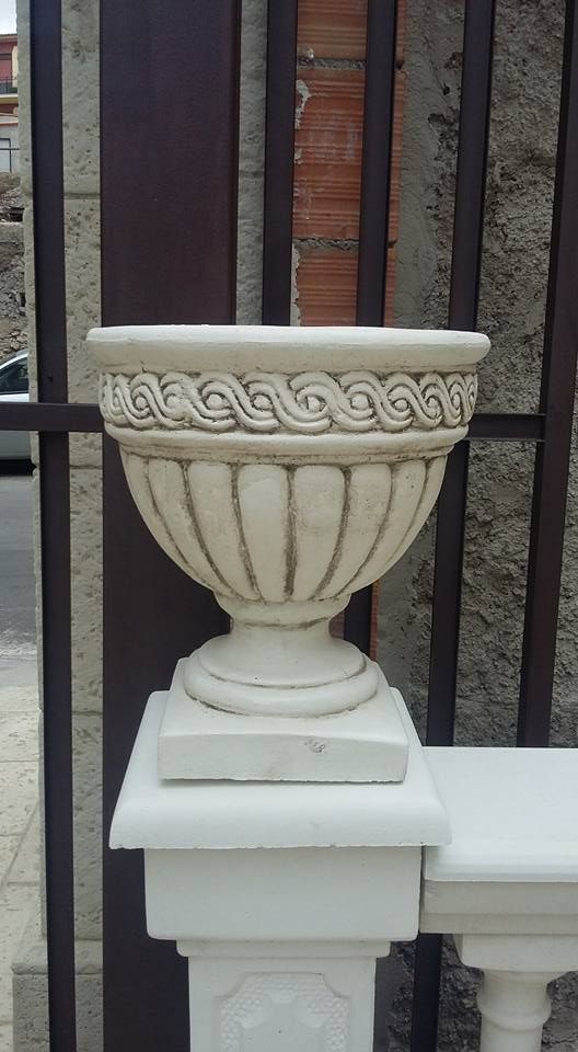 Un'urna decorativa in pietra bianco, con base scanalata e bordo intrecciato, in cima a un pilastro bianco della balaustra.