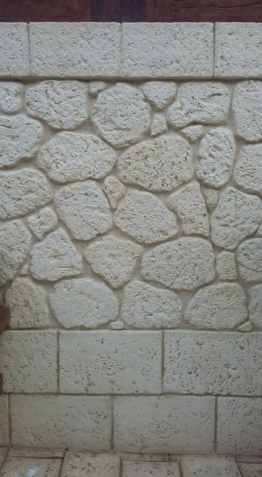 Una parete verticale caratterizzata da una facciata in pietra chiara e strutturata, con una sezione di pietre arrotondate.