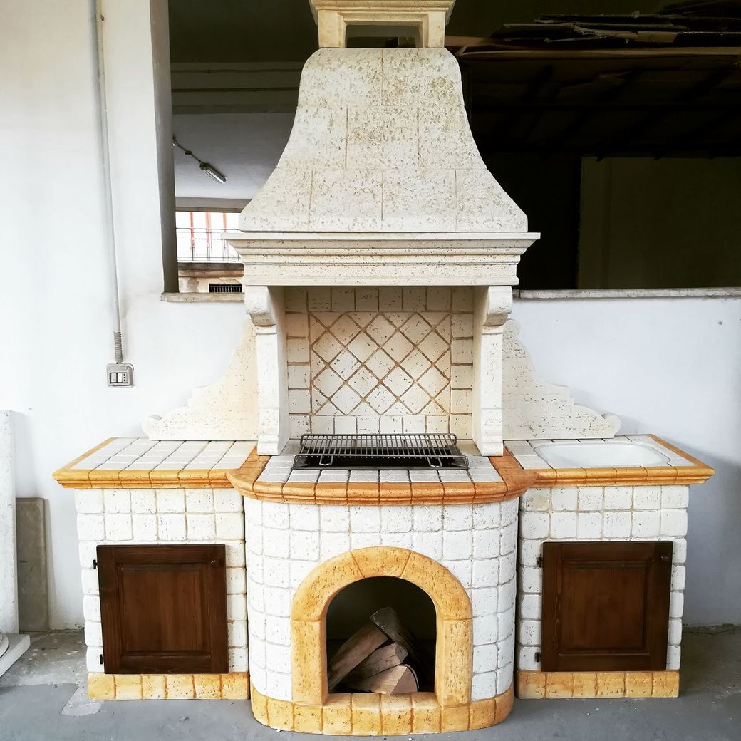 Un barbecue in pietra da esterno con una grande cappa, superfici piastrellate, sportelli in legno e un angolo ad arco.