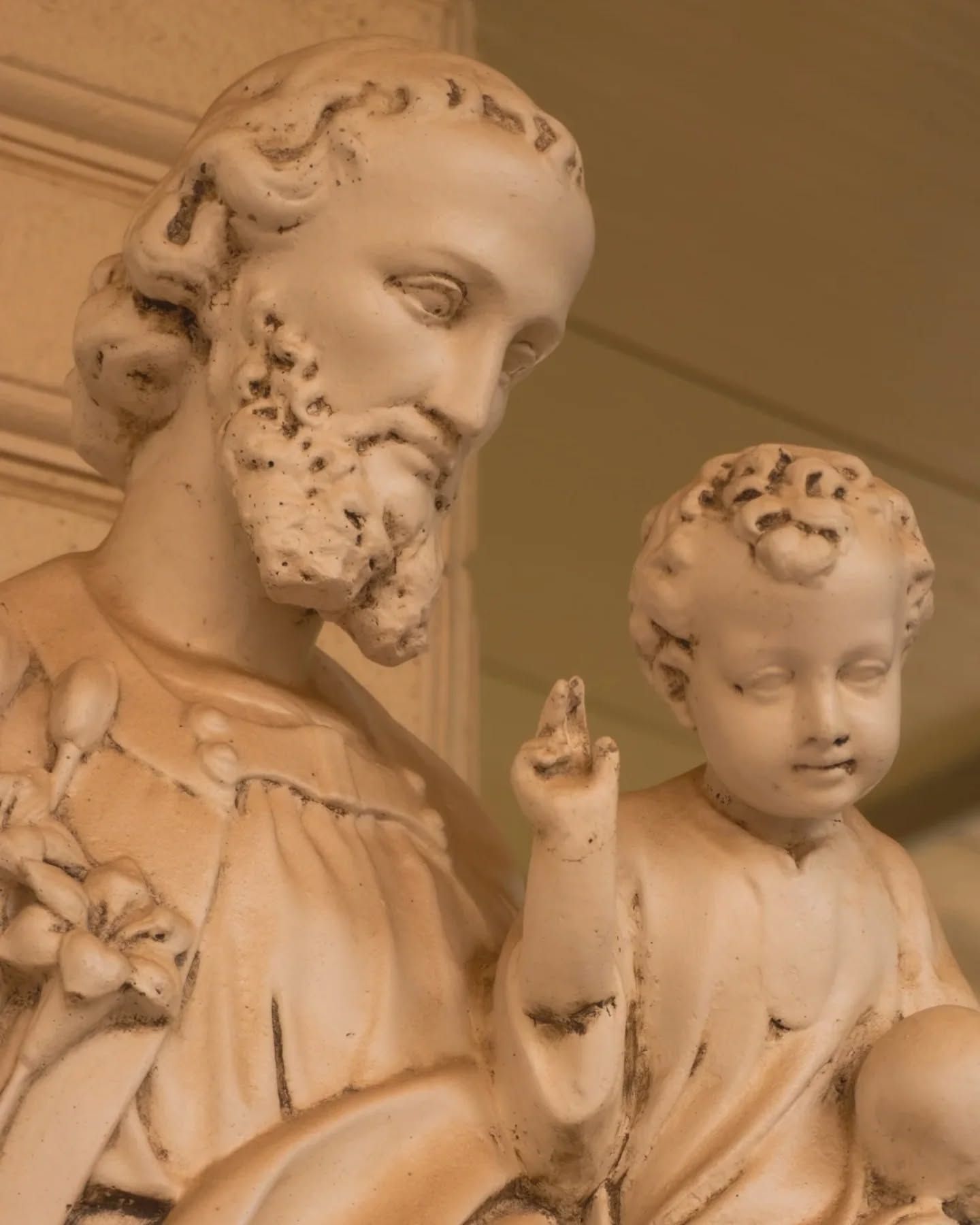 Una statua in marmo bianco raffigurante un uomo barbuto che tiene in braccio un bambino con una mano alzata.