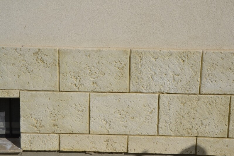 Rivestimento rettangolare in pietra beige chiaro installato con un motivo a correre su una base a muro, con stucco liscio .