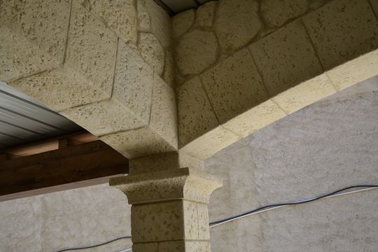 Colonna architettonica beige e angolo con trave, con finitura testurizzata simile alla pietra, contro una parete semplice.