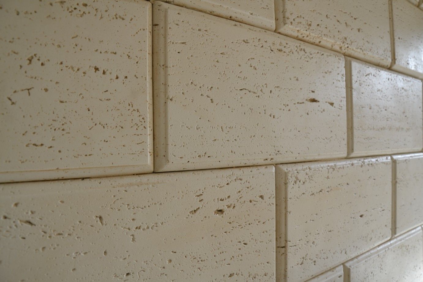 Primo piano di un muro costruito con blocchi di pietra beige chiaro, testurizzati, disposti secondo uno schema a correre.