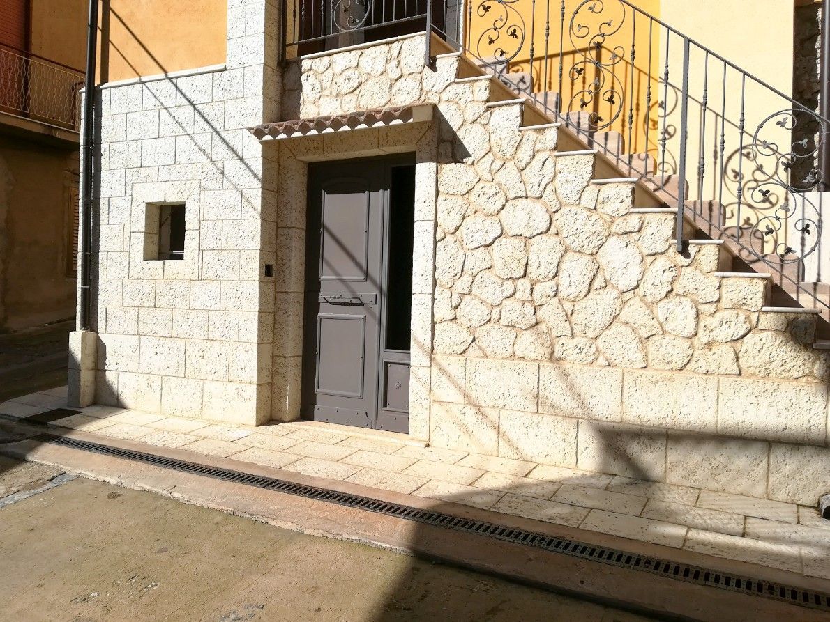 L'esterno di un edificio in pietra con una porta scura, una piccola finestra e una scala in pietra con ringhiera in ferro.