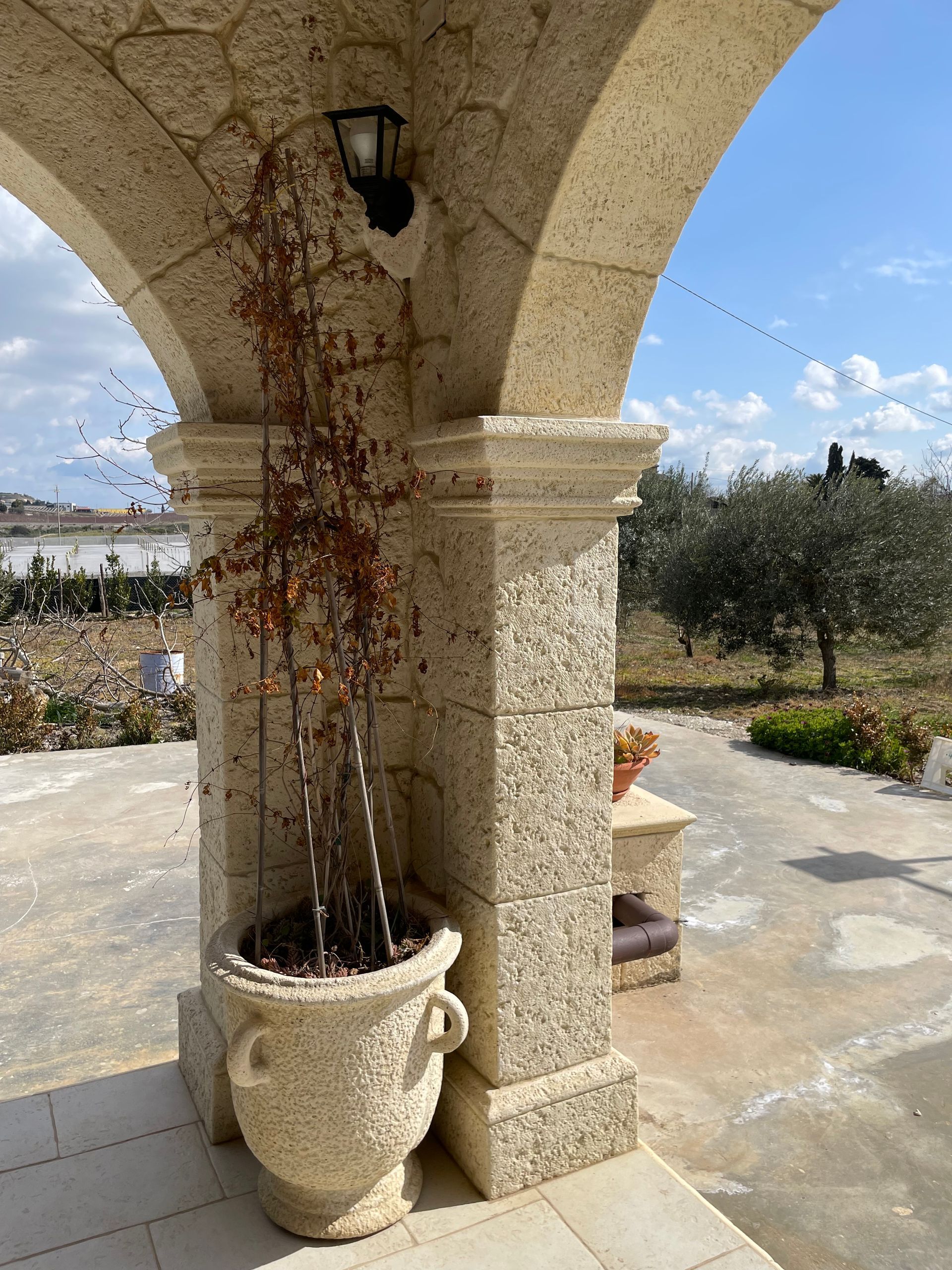 Di fronte a un muro di pietra si trova un pilastro di pietra, con una fioriera decorativa, una panchina di pietra e fiori