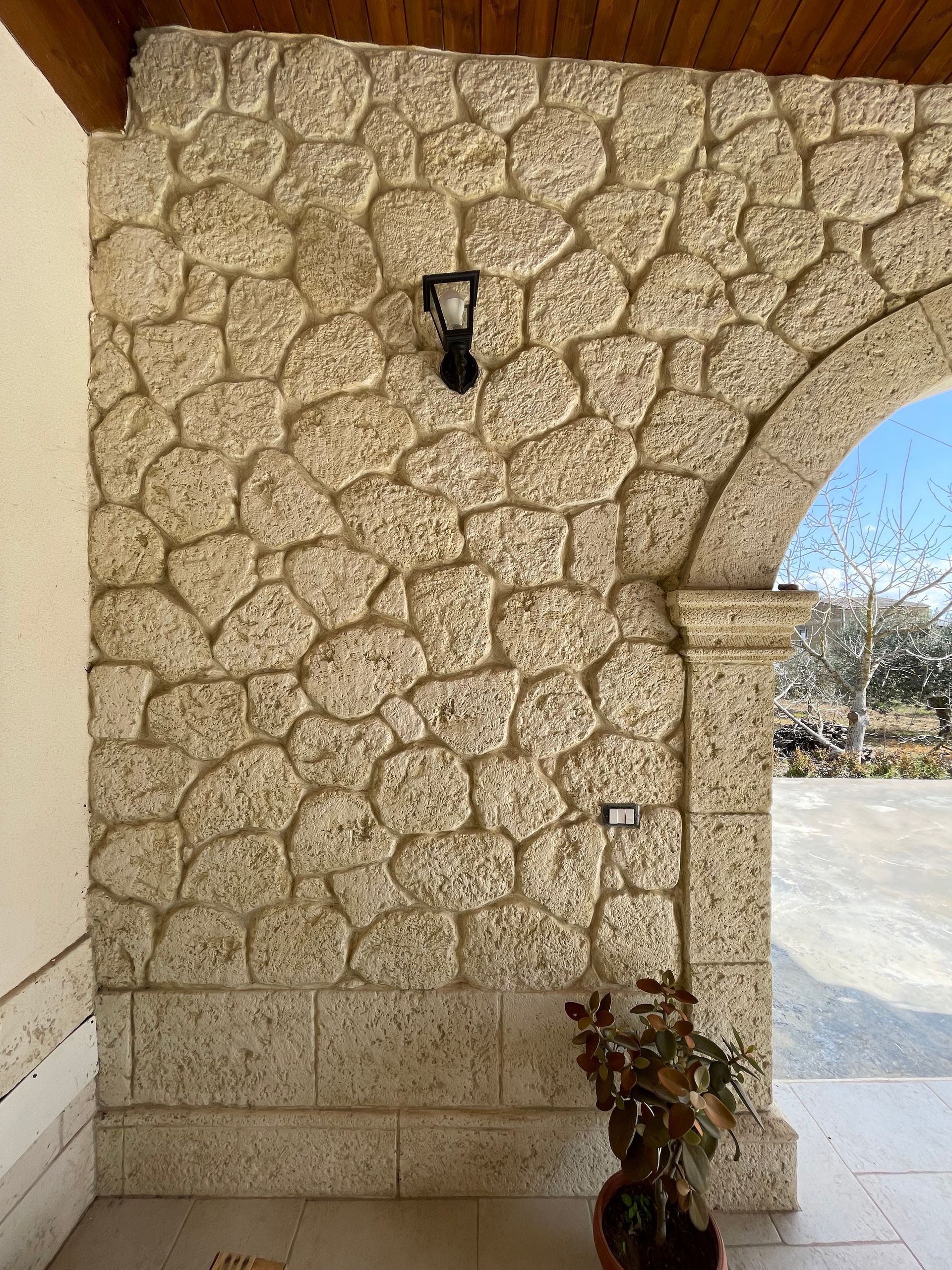 Patio coperto in pietra con colonne e muratura, che si affaccia su uno spazio esterno sotto una struttura in legno.