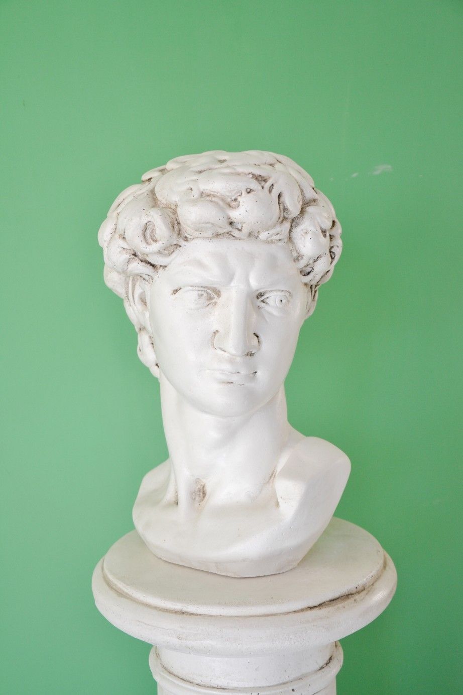 Busto in marmo bianco raffigurante una figura classica, con capelli ricci e un'espressione neutra, su un piedistallo.