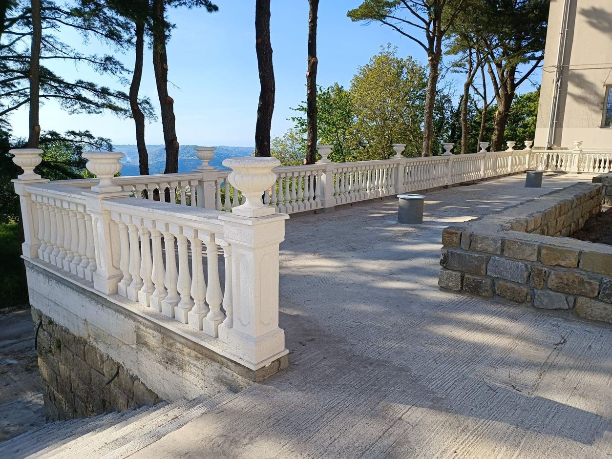 Una balaustra in pietra su un patio rivestito di tegole rosse, con impalcature sulla sinistra e alberi sullo sfondo .