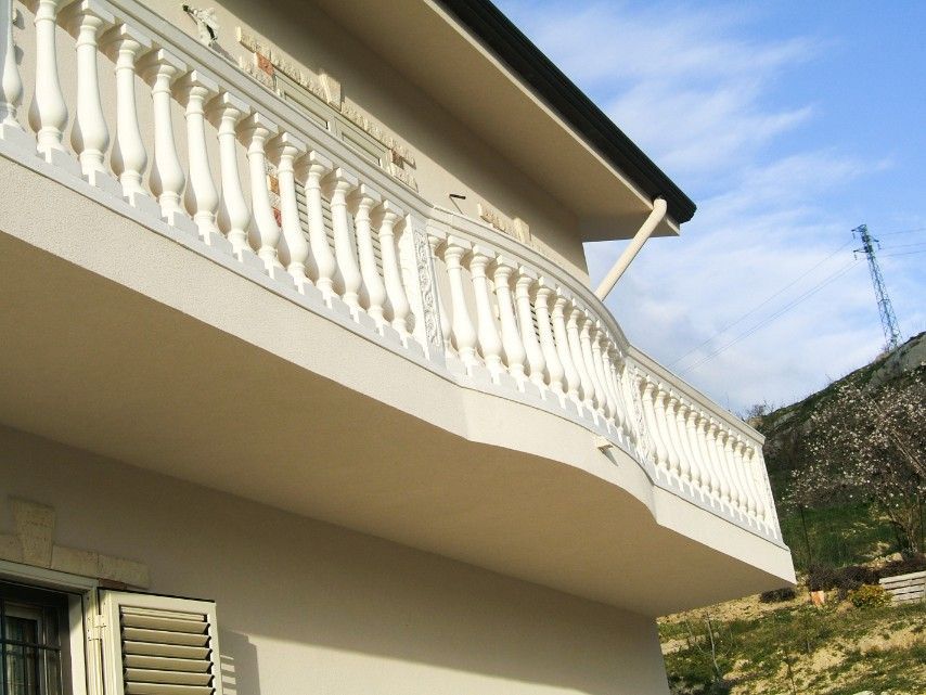 L'esterno di un edificio beige è caratterizzato da un balcone curvo con balaustre bianche sotto un cielo limpido.