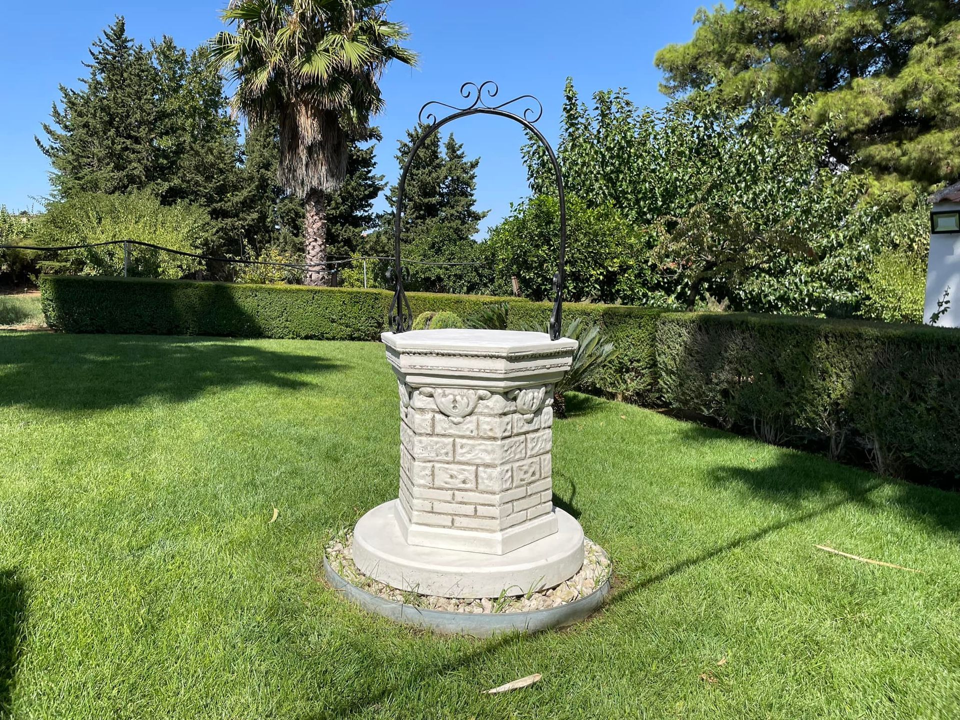 Un pozzo decorativo da giardino in pietra con un arco in metallo, situato su un rigoglioso prato verde in un giardino .