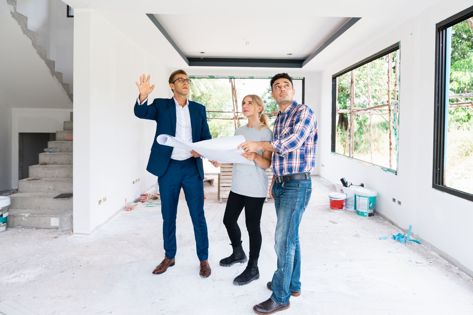 A man and a woman are standing in an empty room looking at a blueprint.