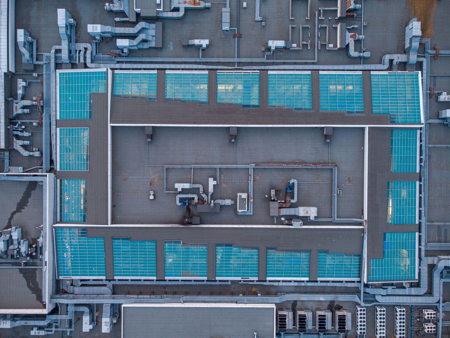 Aerial view of a large rooftop with teal panels and industrial equipment in the center.