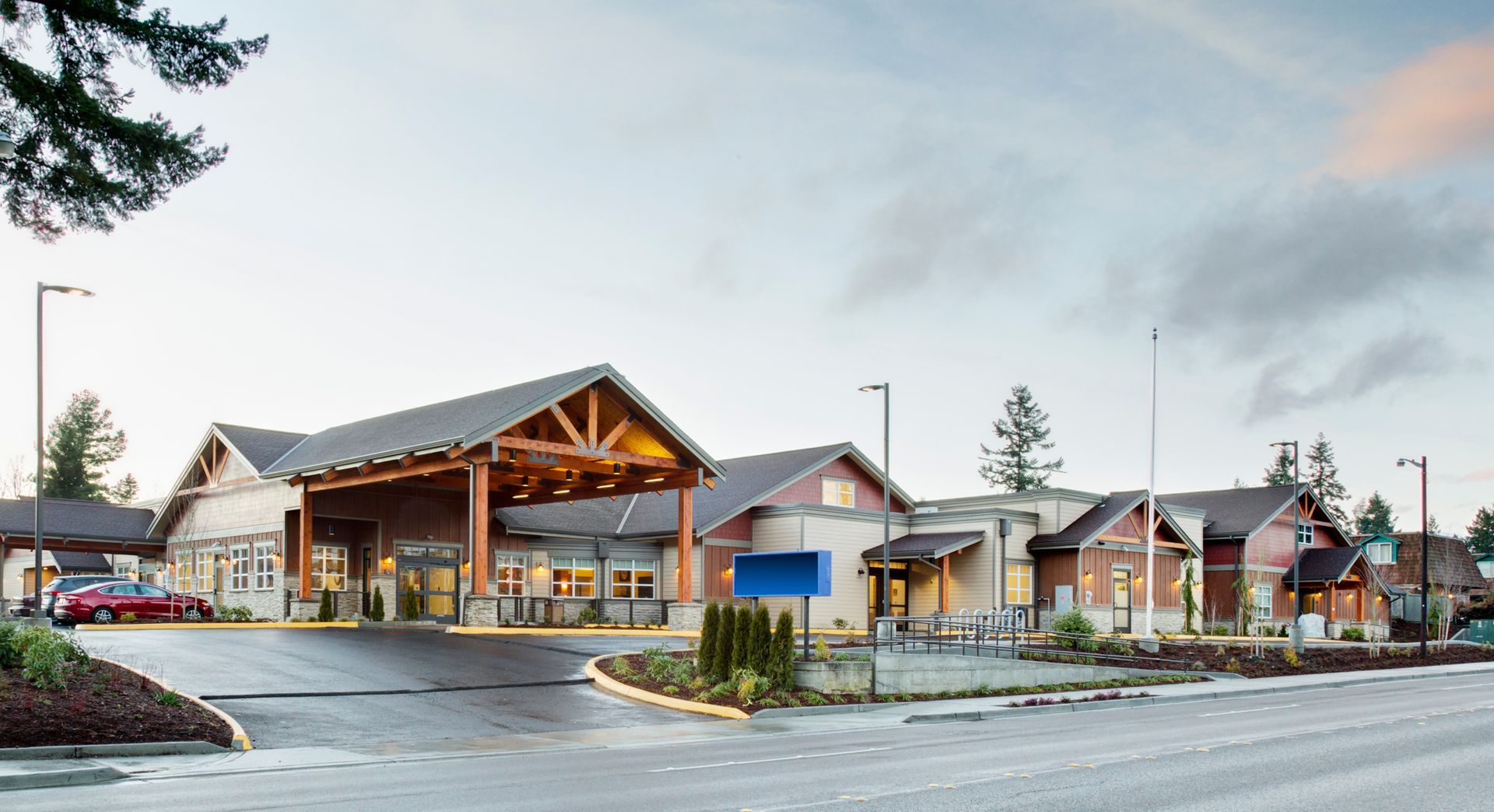 Modern building with a large wooden entrance canopy in a paved parking lot at dusk