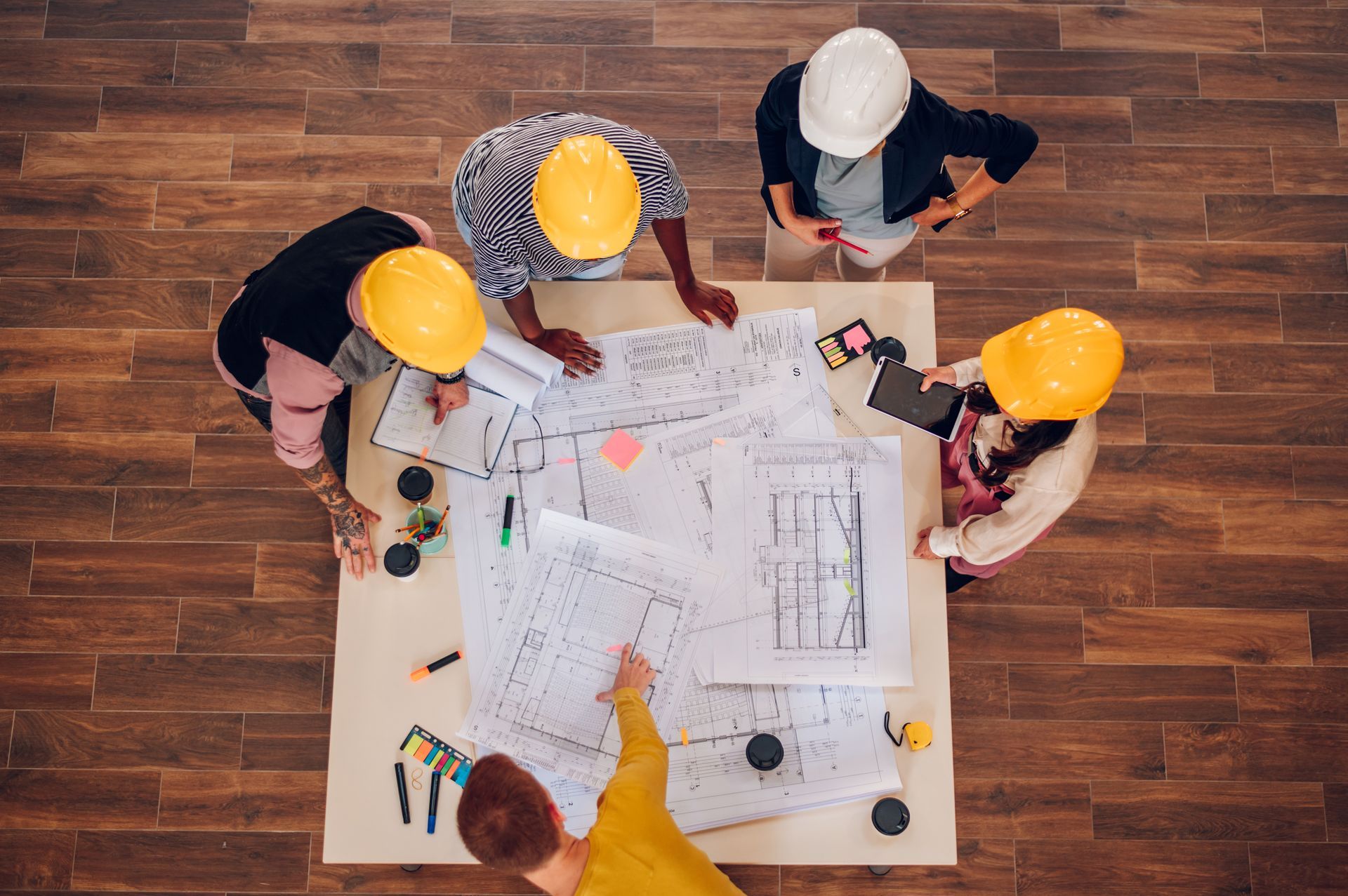 Team of workers in hard hats reviewing blueprints around a table on a construction site