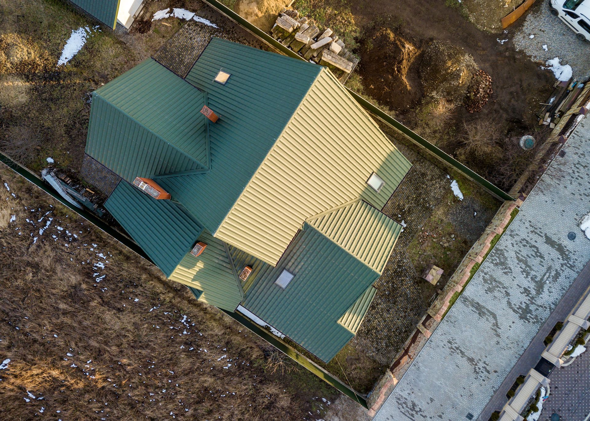 Aerial view of a house with green and tan roof beside a road and snowy ground