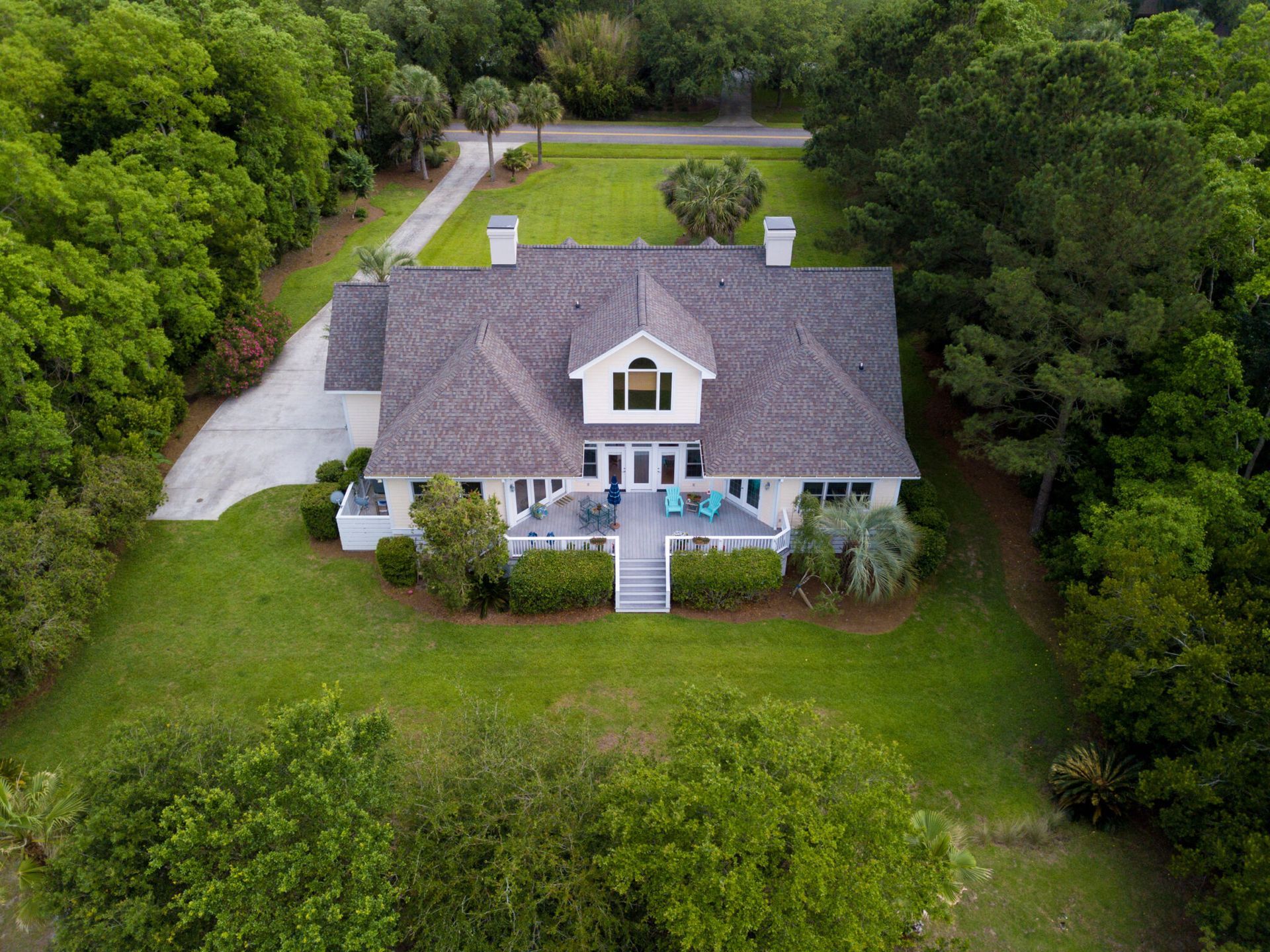 Aerial view of a gray house with a front porch, surrounded by dense green trees and lawn.