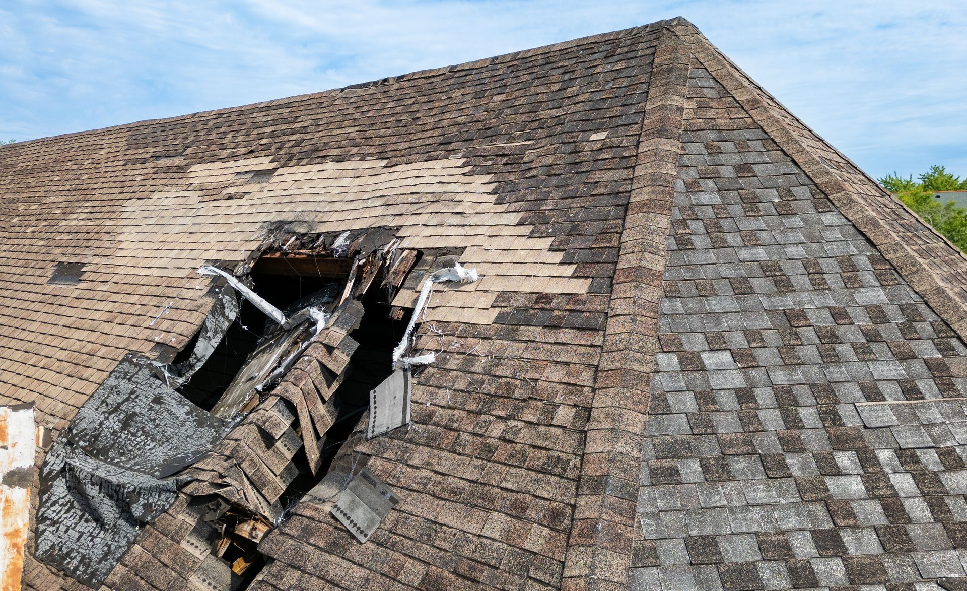 Collapsed roof with a large hole and exposed beams on a shingled house