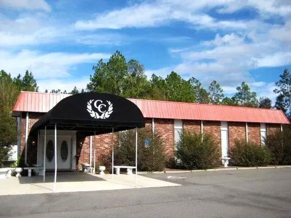 Front entrance of a brick building with a black awning and red metal roof, surrounded by trees under a blue sky