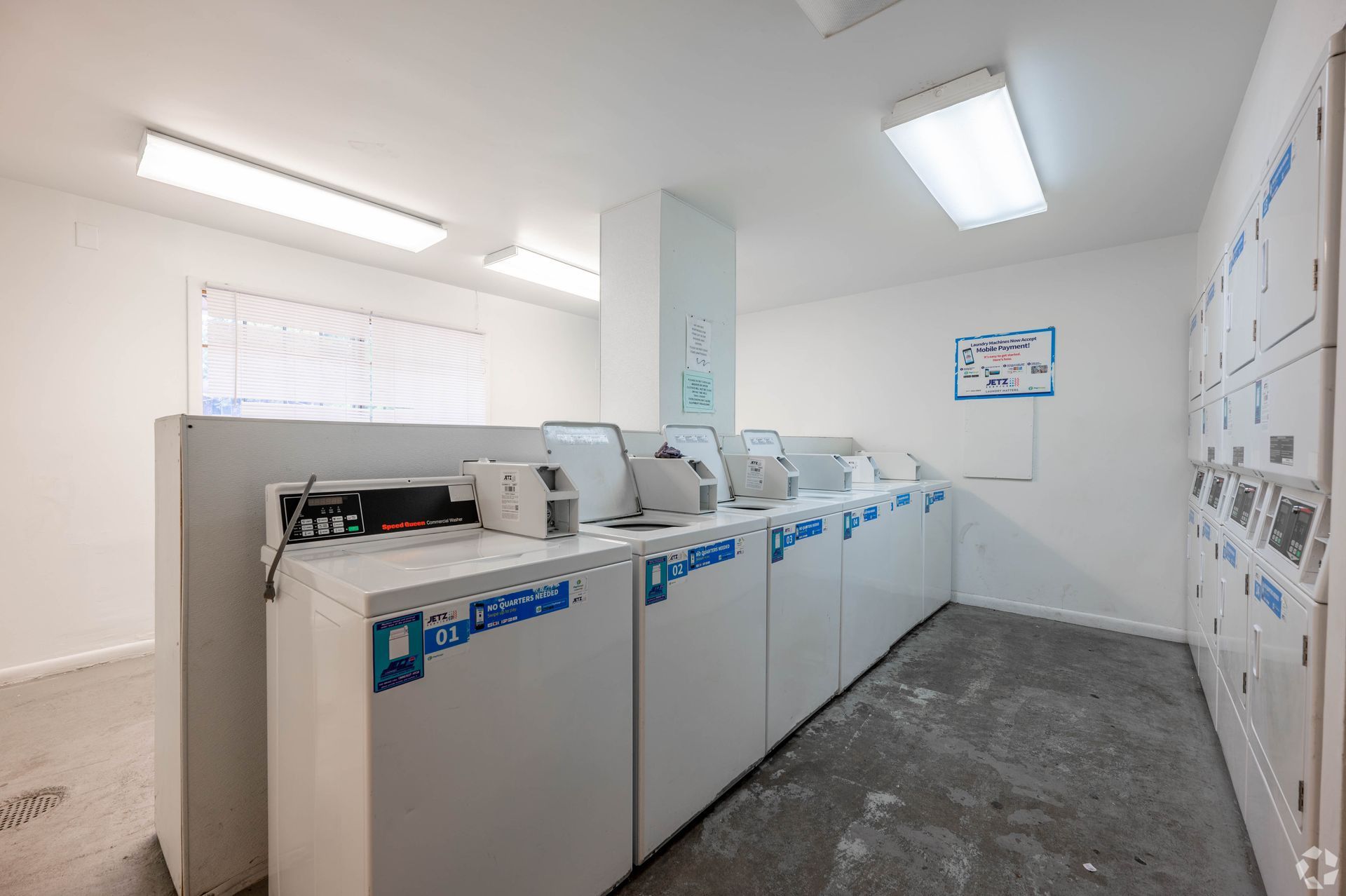 Laundry room with white washing machines, concrete floor, and bright overhead lights.