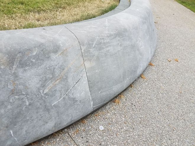 Curved concrete planter wall bordering grass and gravel path with visible cracks