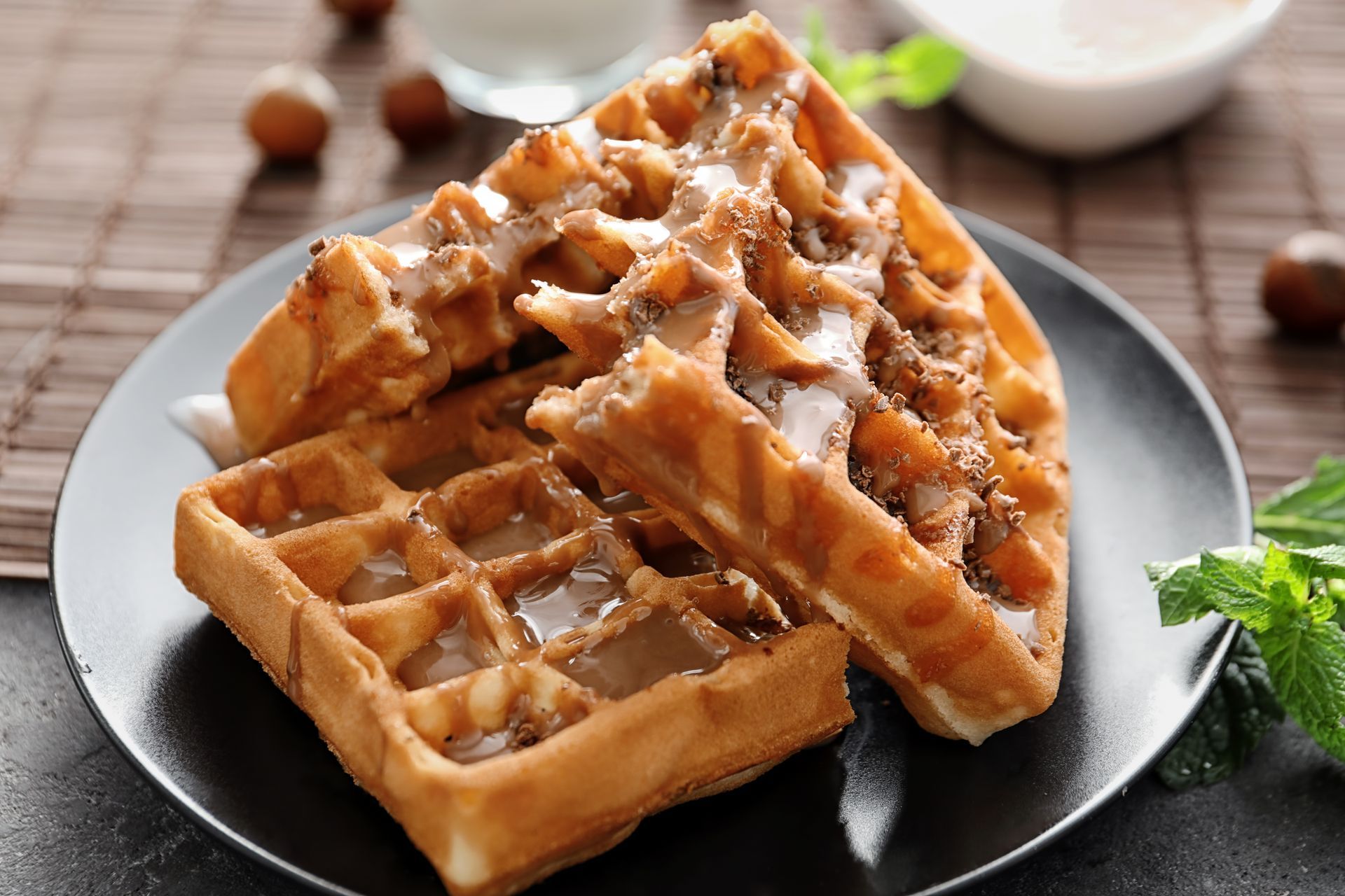 Three waffles on a black plate, drizzled with glaze.