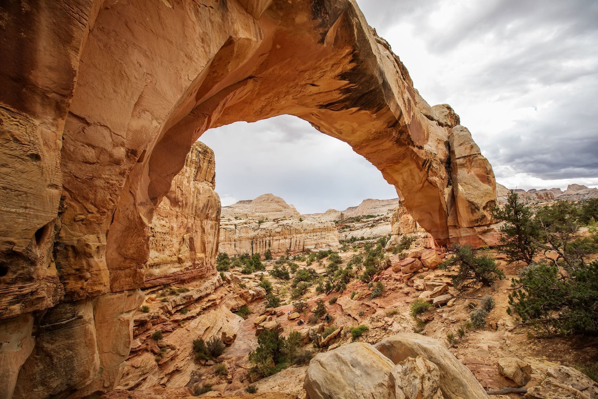 Natural stone archway in canyon landscape, with view of distant cliffs and cloudy sky.