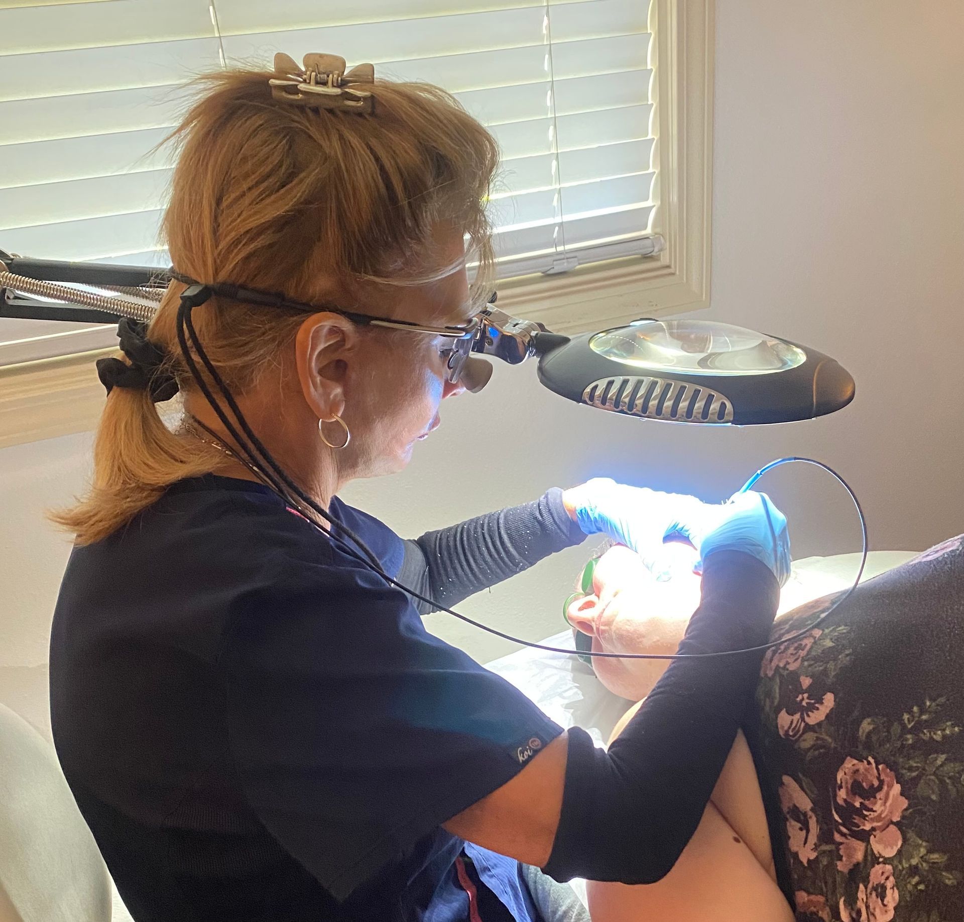 A clinician in gloves applies a laser treatment to a reclining patient wearing protective goggles.