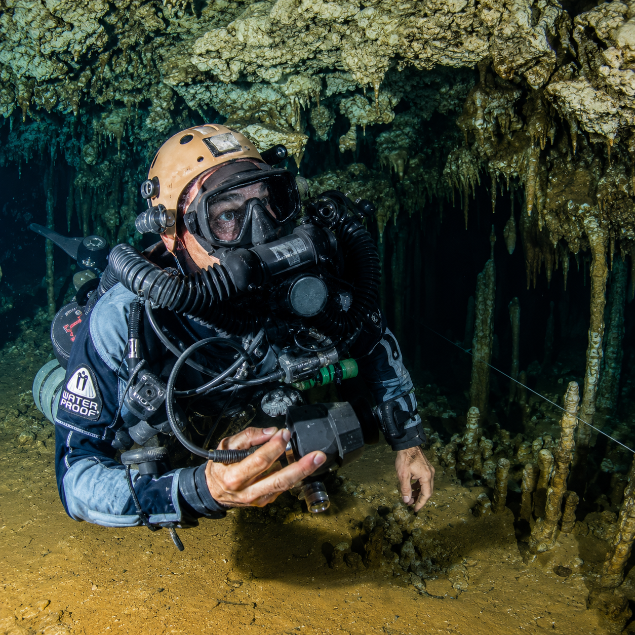 Scuba diver in black gear explores an underwater cave with stalactites and murky water