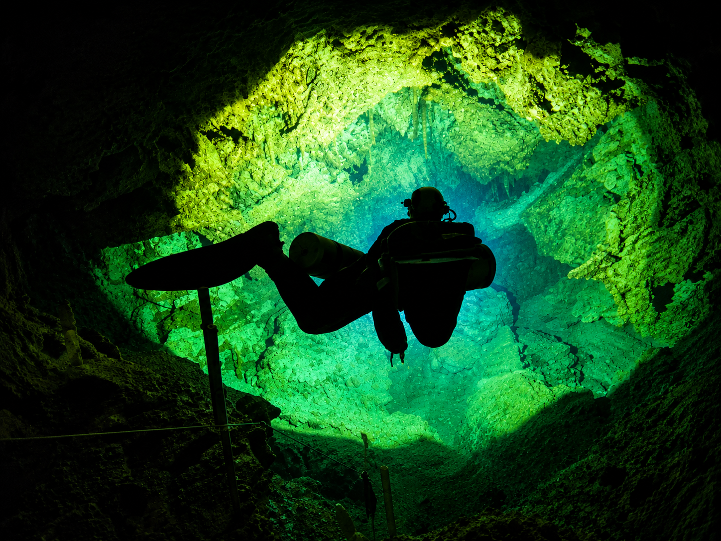 Silhouette of a scuba diver underwater in a glowing green cave