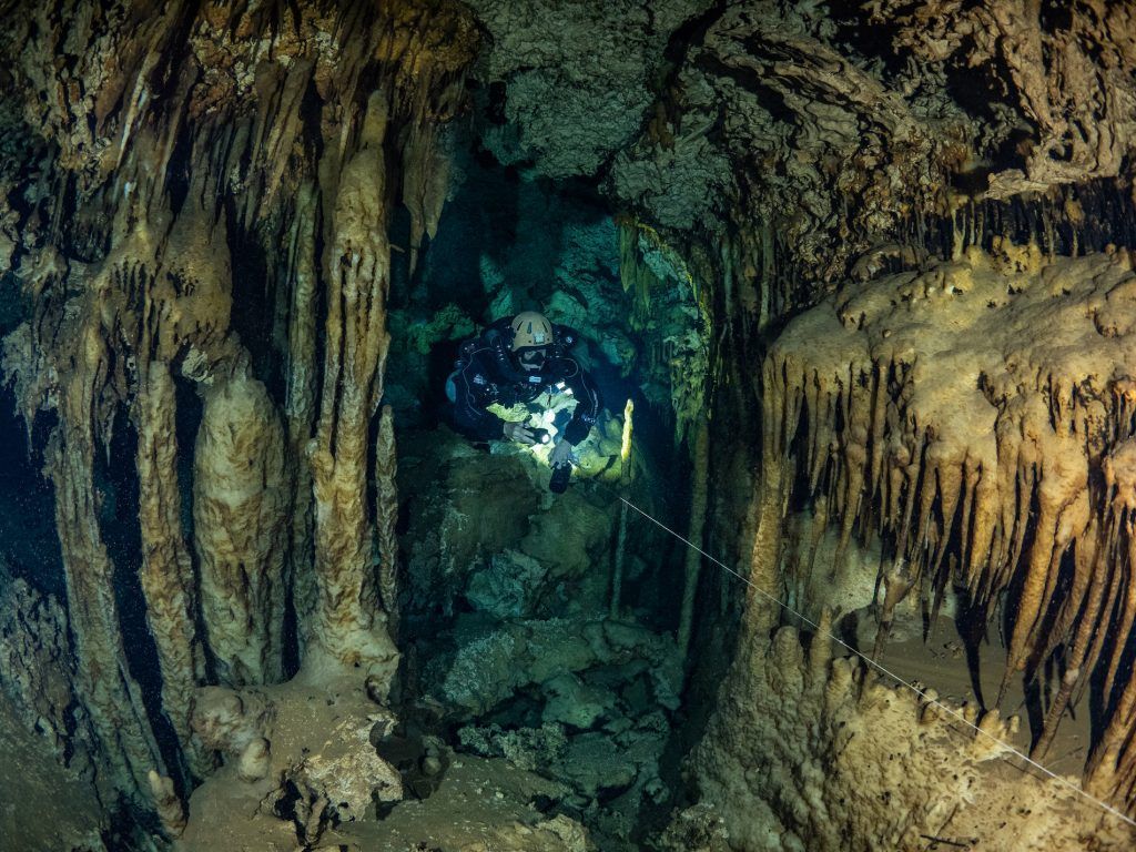 Narrow cave tunnel with rough rock walls and a small blue-lit opening in the distance