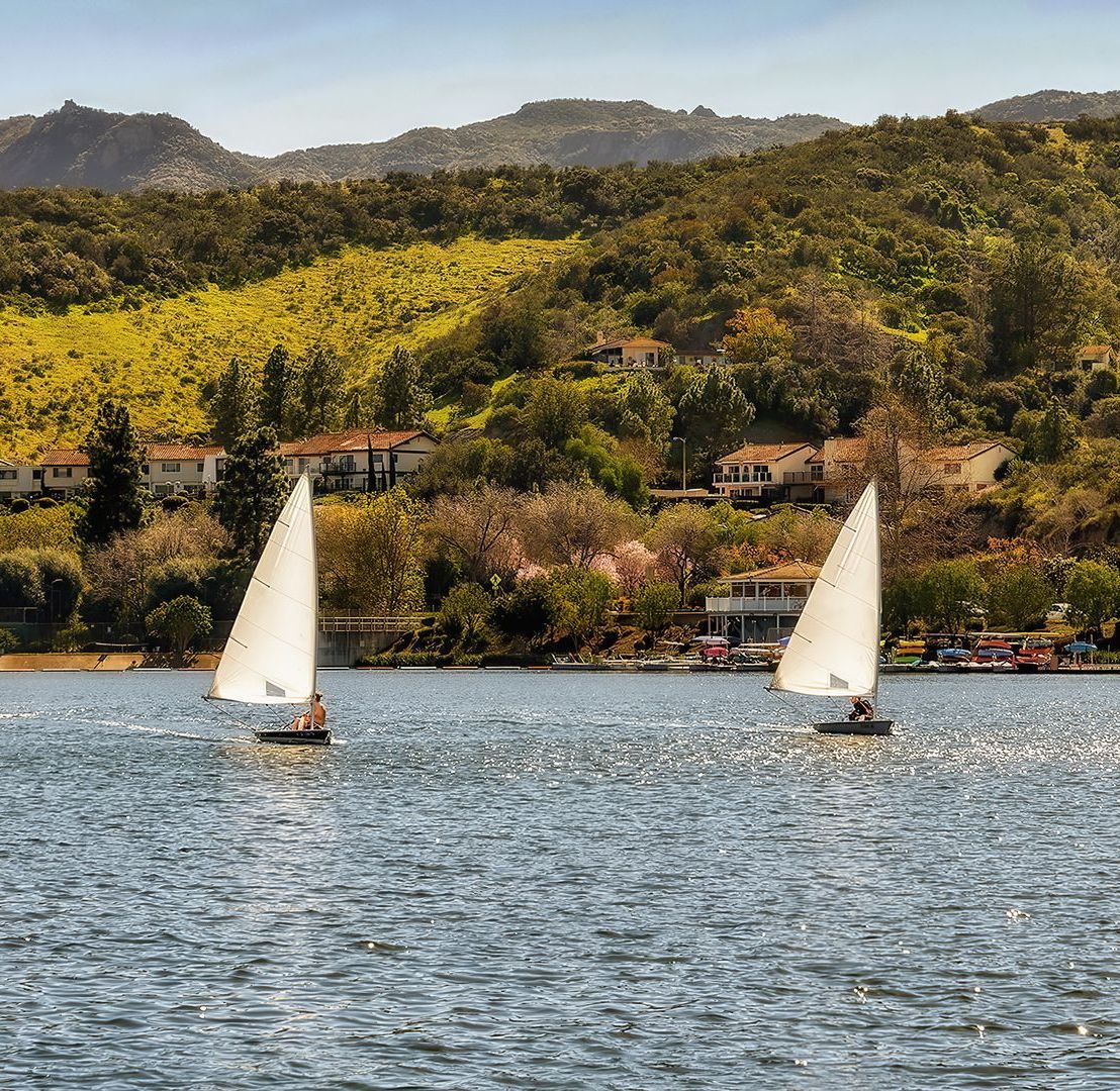 Two sailboats are floating on a lake with mountains in the background