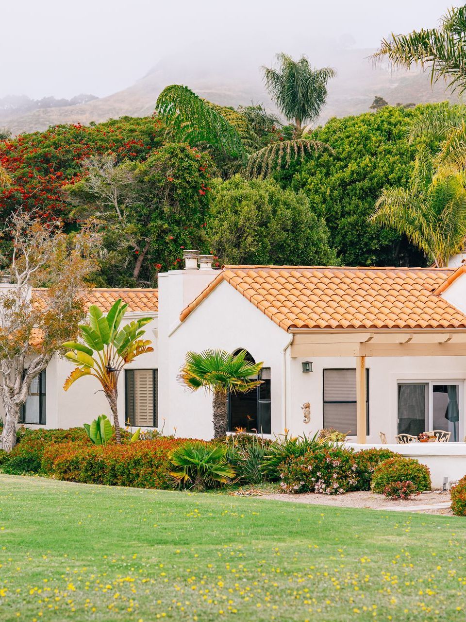 A white house with a tiled roof and a lush green lawn in front of it.