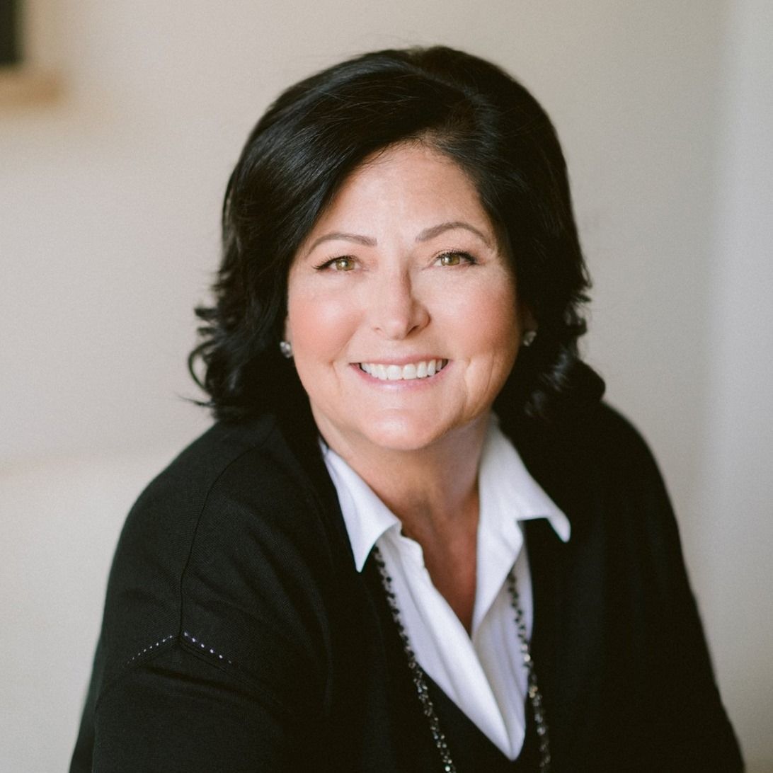 Portrait of a smiling person in a black sweater and white collared shirt against a soft beige background