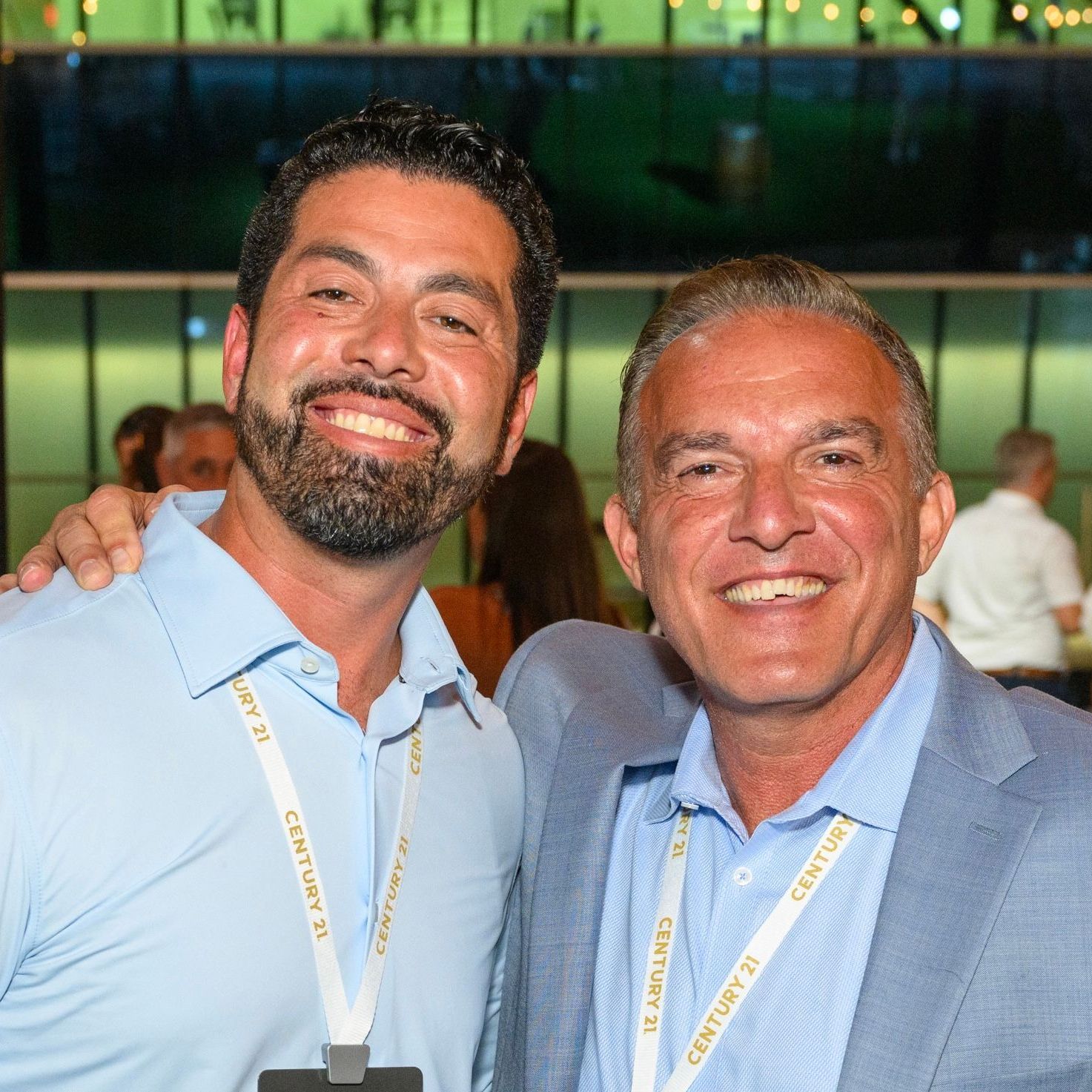 Two men are posing for a picture and one has a century 21 lanyard around his neck